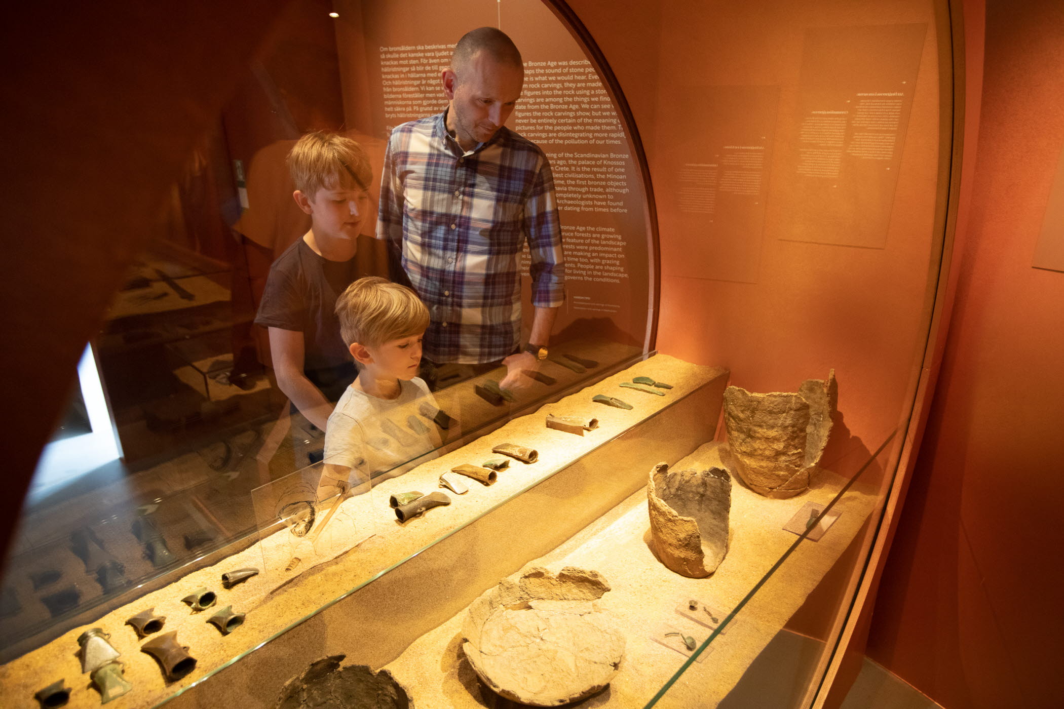 Två barn och en vuxen tittar in i en monter i utställningen Vägen hit.